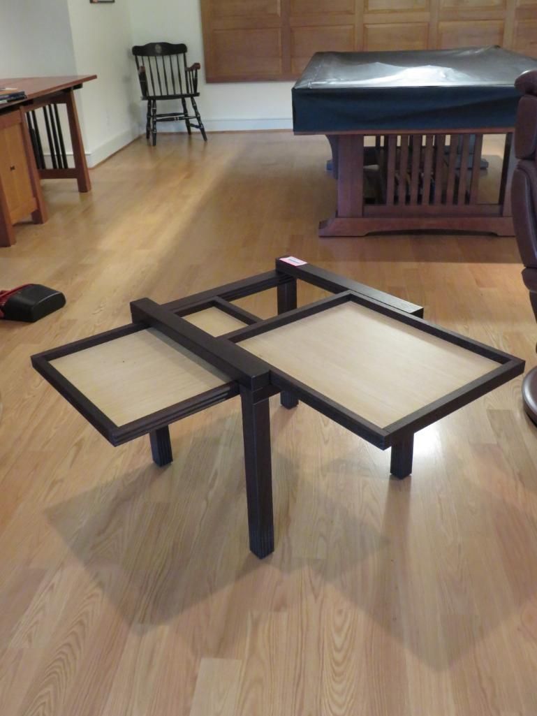 A dark wood expandable coffee table with two leaves open, sitting on a wooden floor in a room.