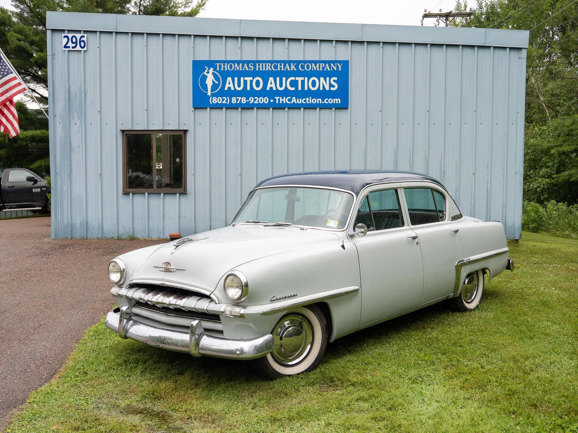 Vintage gray and black sedan parked in front of an auto auction building.