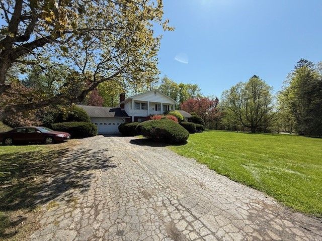 A two-story white house with a cracked driveway, lawn, and a car parked on the side.