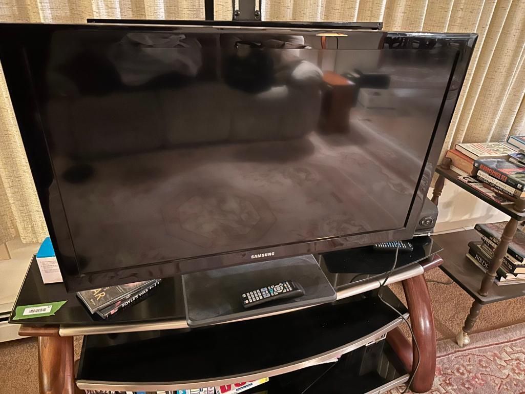 A black flat-screen TV on a wooden and glass stand, with remote control visible.