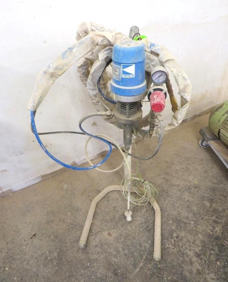 A paint sprayer on a stand with a blue motor and pressure gauge, in a room with a concrete floor.