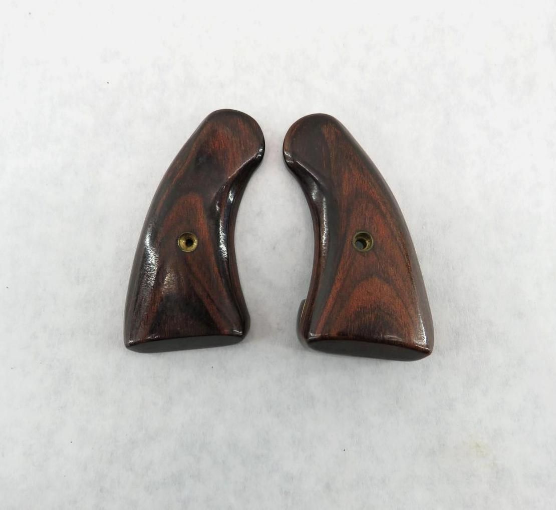 Two dark wooden handgun grips with brass inserts, against a white background.