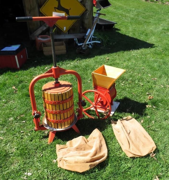 Apple press and grinder with bags on grass. Red and yellow equipment, outdoors.
