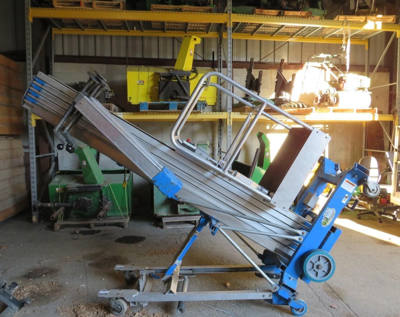 Blue and gray lift in a warehouse, angled upward. It has wheels, and a guardrail.