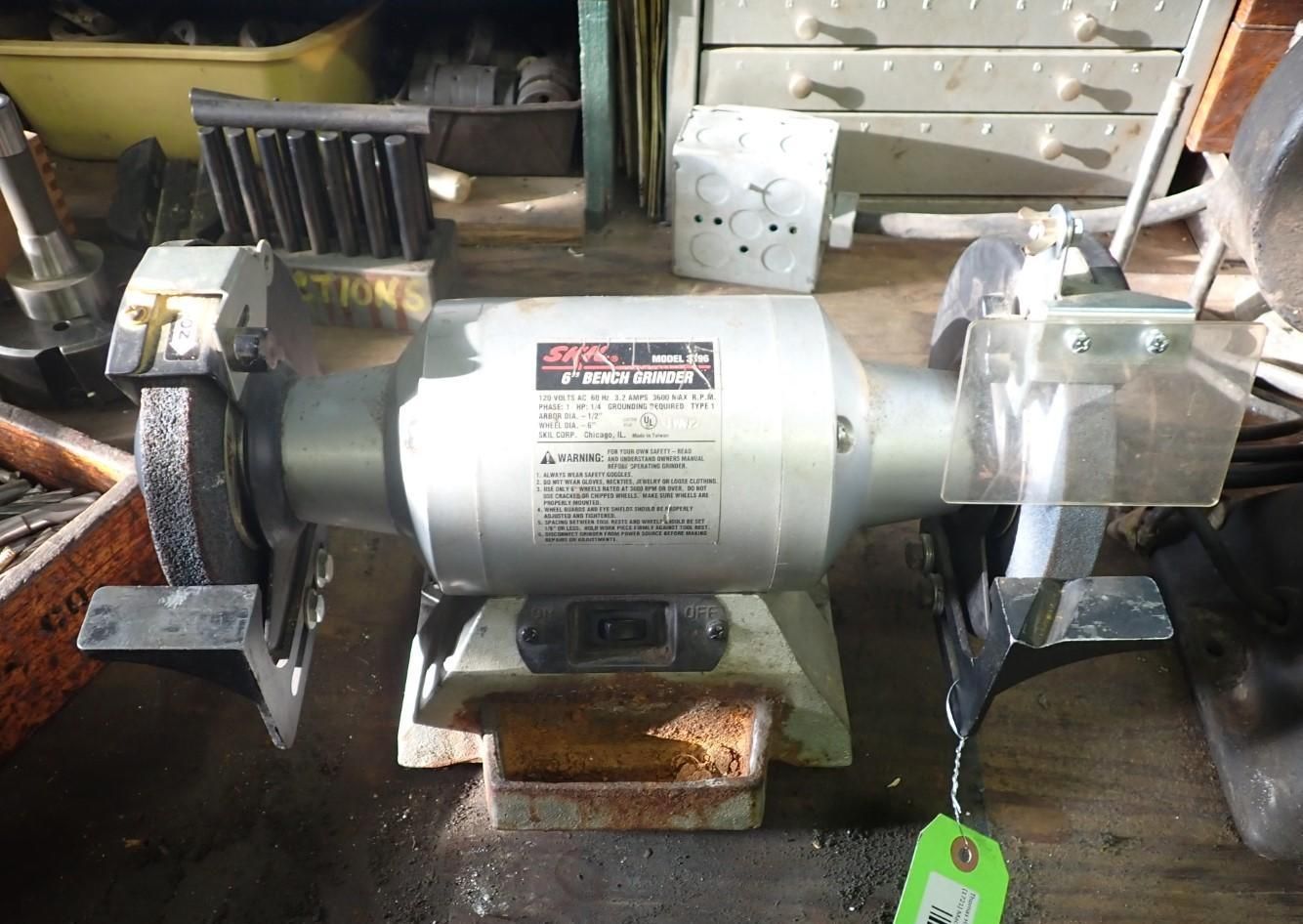 A bench grinder with a silver motor and two abrasive wheels sits on a workbench.