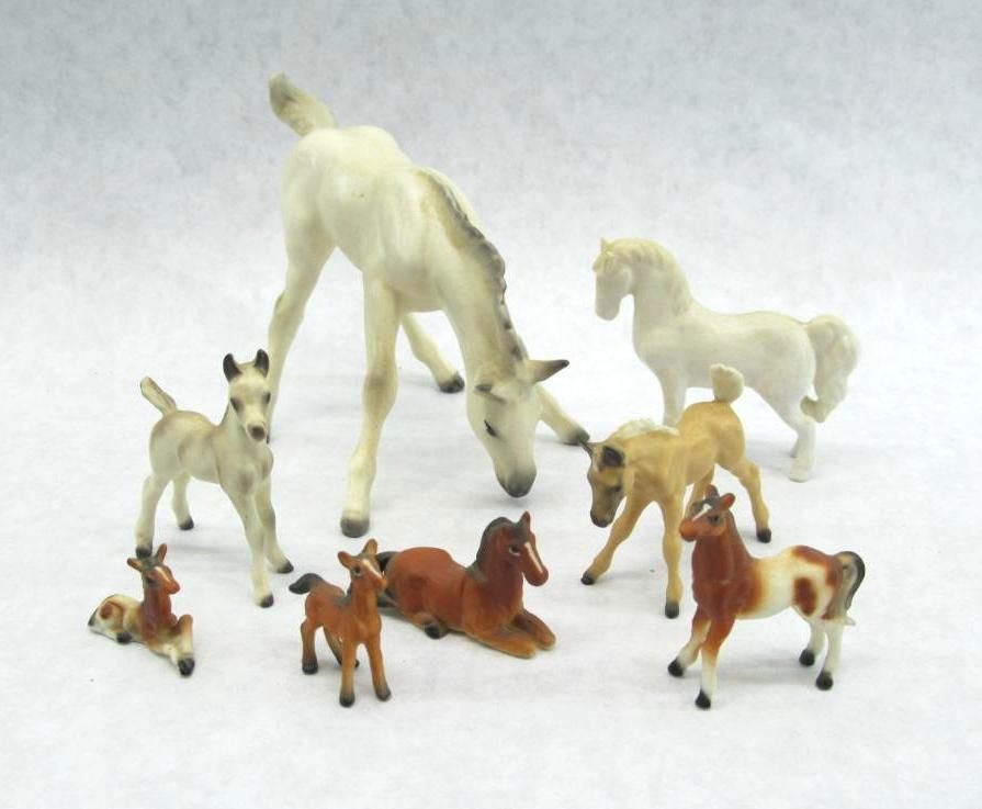 Miniature toy horses in various colors and poses, including standing, lying down, and grazing, on a white surface.