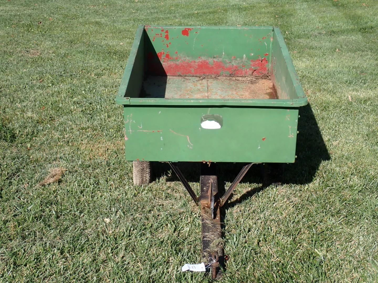 Green metal farm spreader on grass, with red interior
