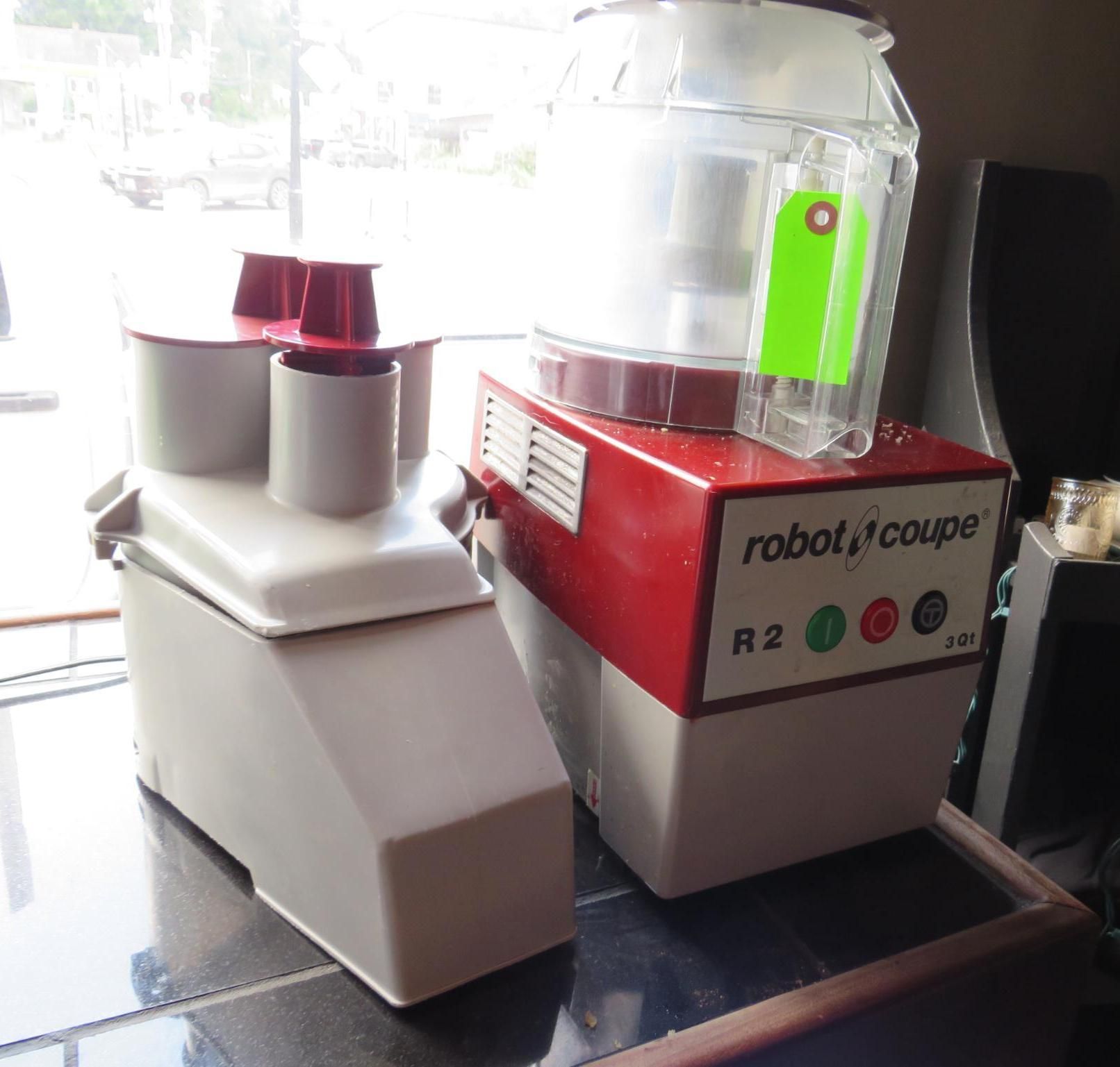 Two Robot Coupe food processors, one white and one red, sitting on a table near a window.