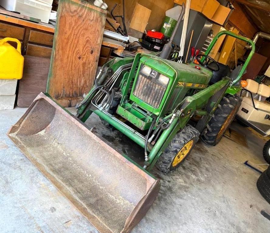 Green John Deere tractor with front loader parked in a garage.