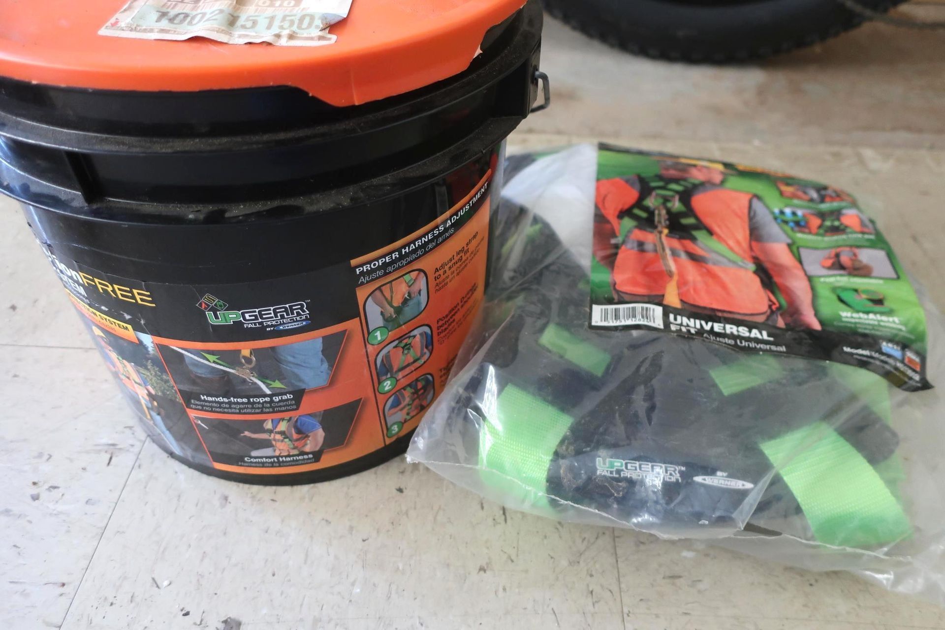 Black bucket with orange lid, next to a packaged green and black safety harness.