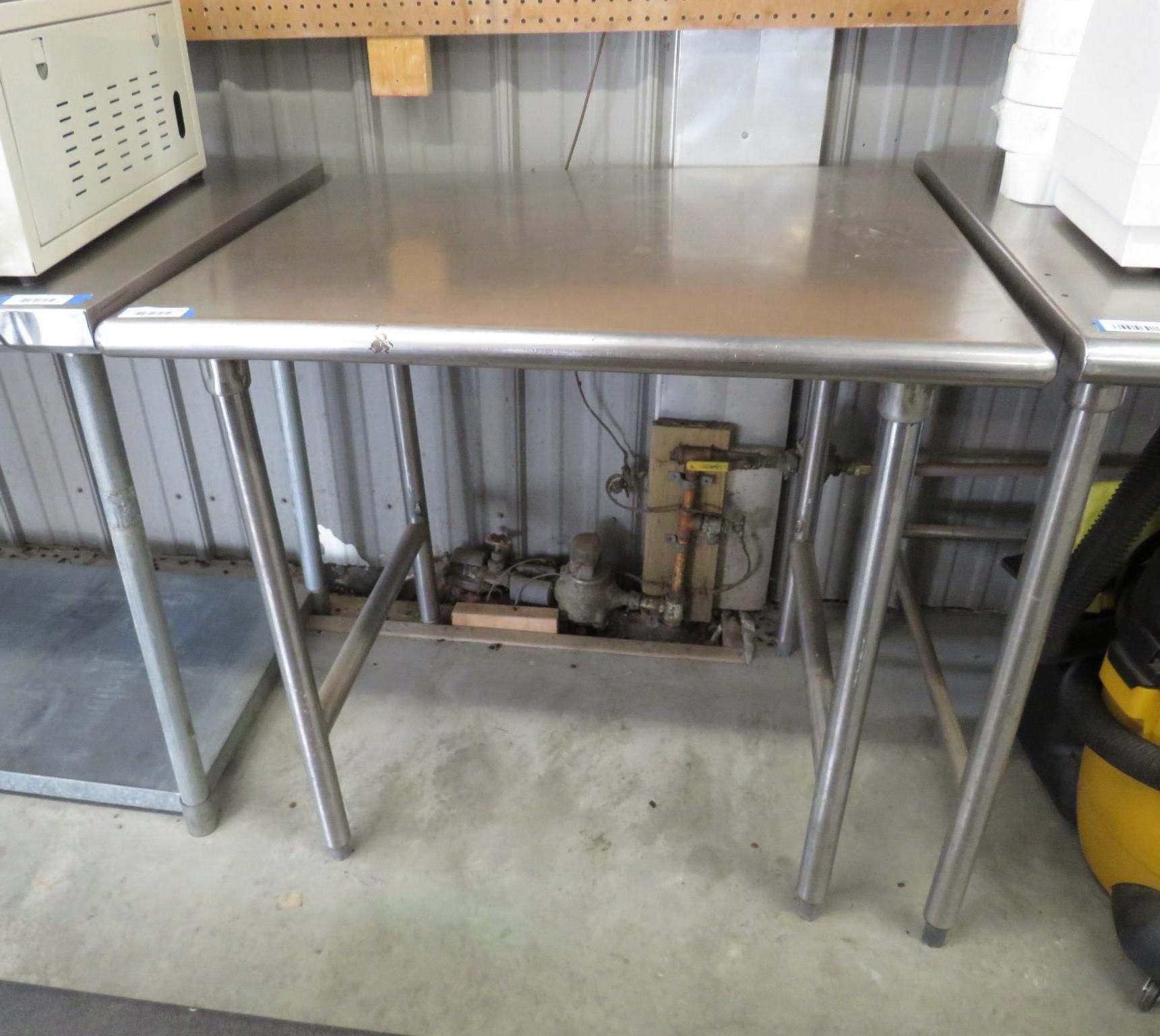 Stainless steel work tables in a room with industrial equipment.