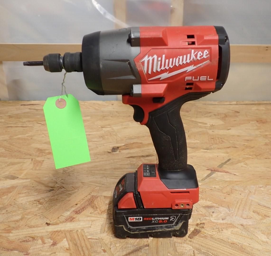 Red and black Milwaukee Fuel impact driver with battery, green tag, sitting on wood surface.