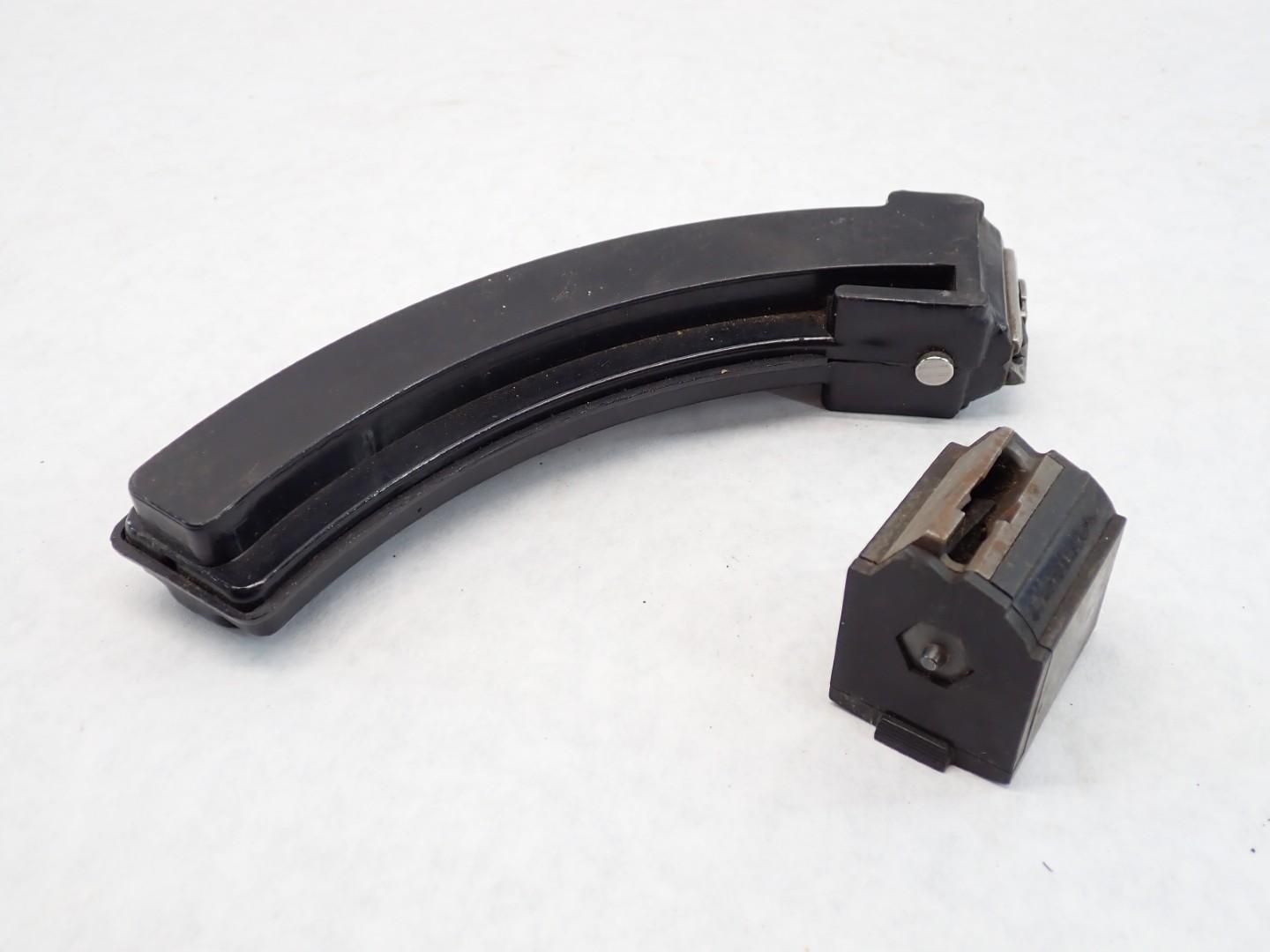 Two black gun magazines on a white surface; one curved, one rectangular.