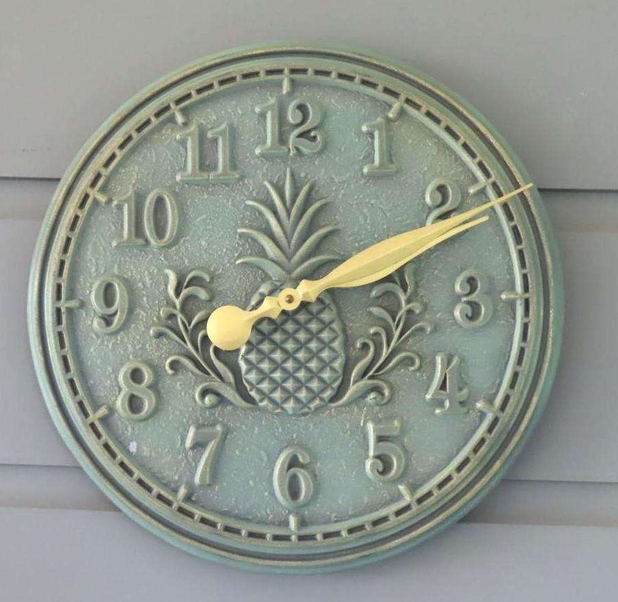 Round outdoor clock, turquoise color with pineapple design in the center, hands pointing to 2:10.