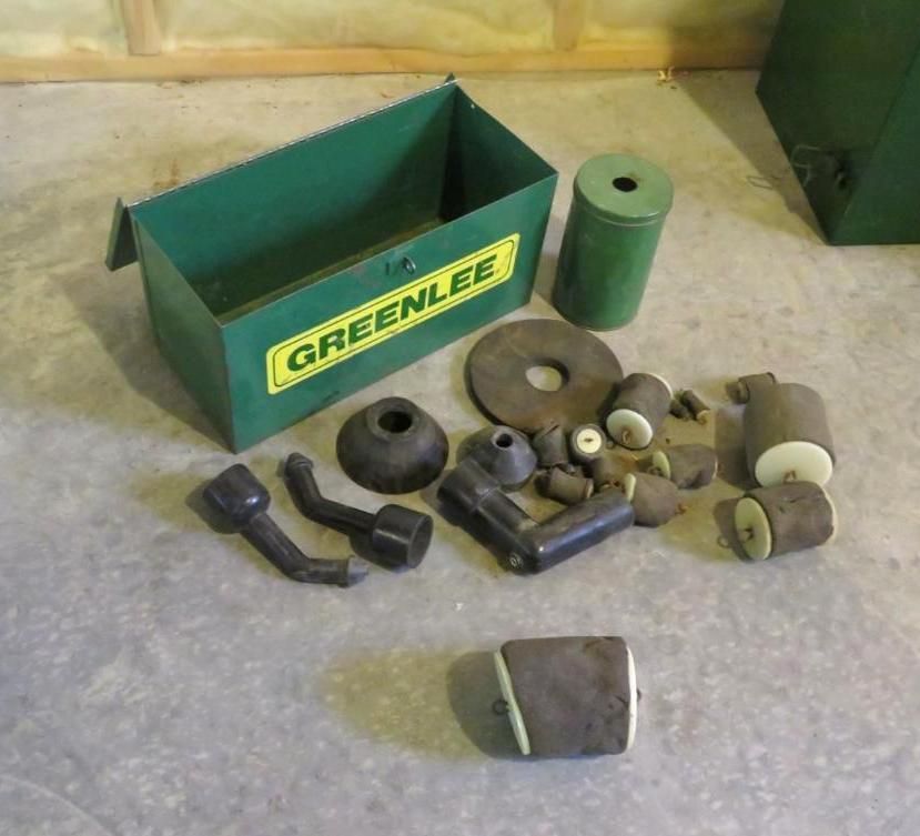 Green Greenlee toolbox and assortment of dark rubber and tan objects on a concrete floor.