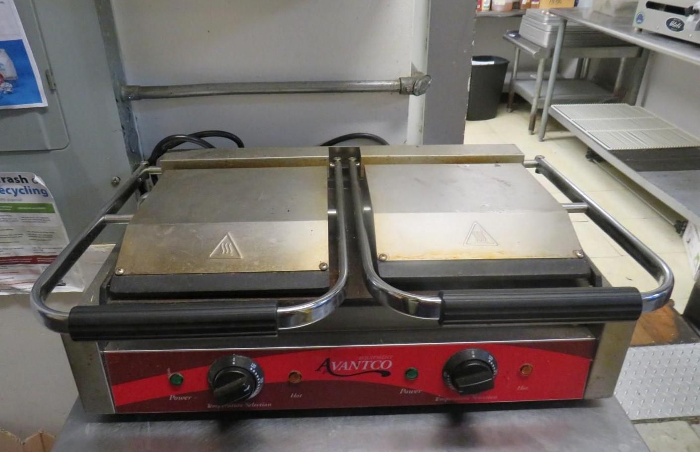 A dual-sided panini press on a red base with black handles.