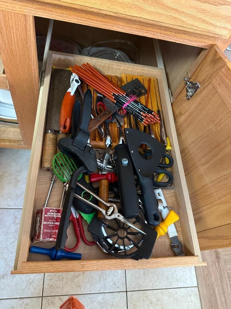 Open wooden drawer filled with various tools, including hammers, scissors, and a whisk.