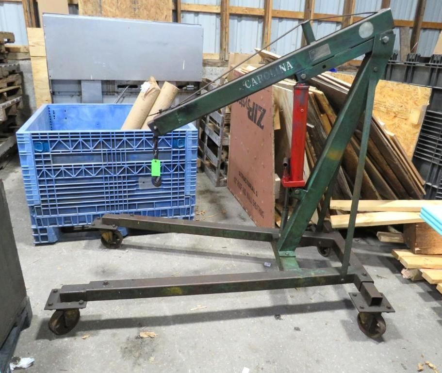 Green engine hoist with a red hydraulic pump, next to a blue bin in a workshop.
