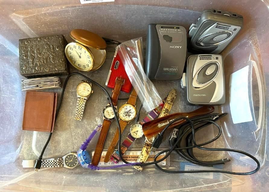 Items in a plastic bin: jewelry box, watches, cassette players, a clock.