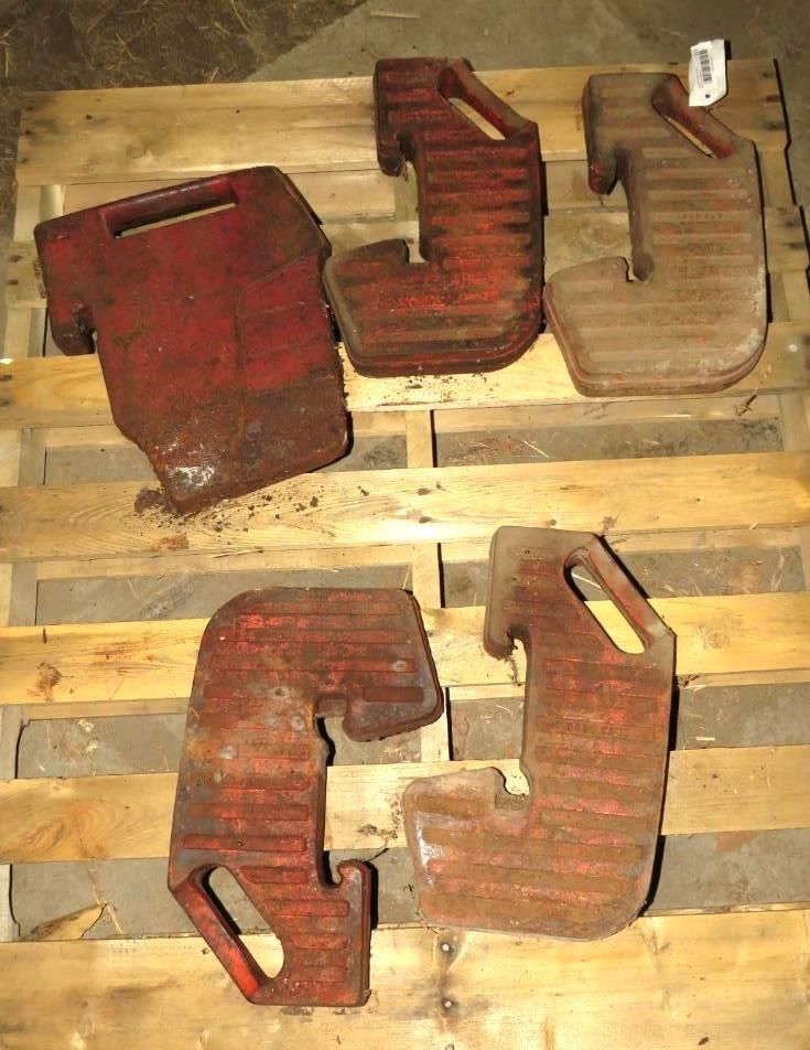 Five red, cast iron tractor wheel weights on a wooden pallet.