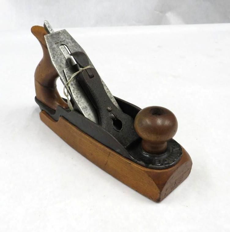 A wooden hand plane with a dark iron blade and wooden handles, resting on a white surface.