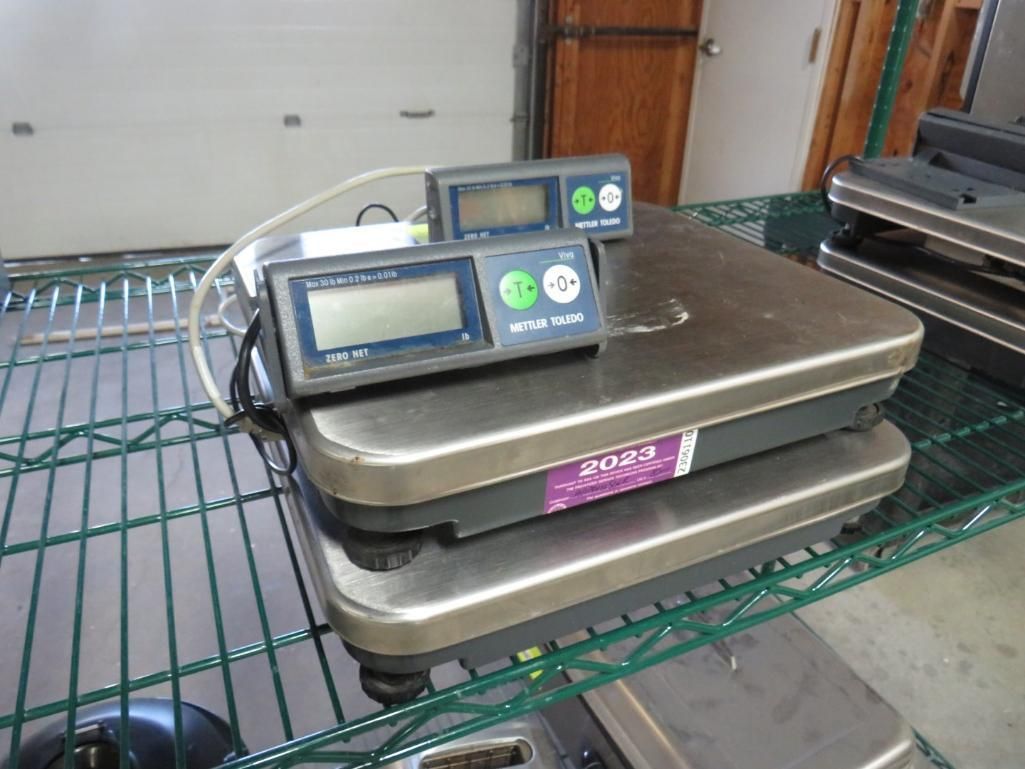 Two digital scales stacked on a metal shelf. One has a purple label.