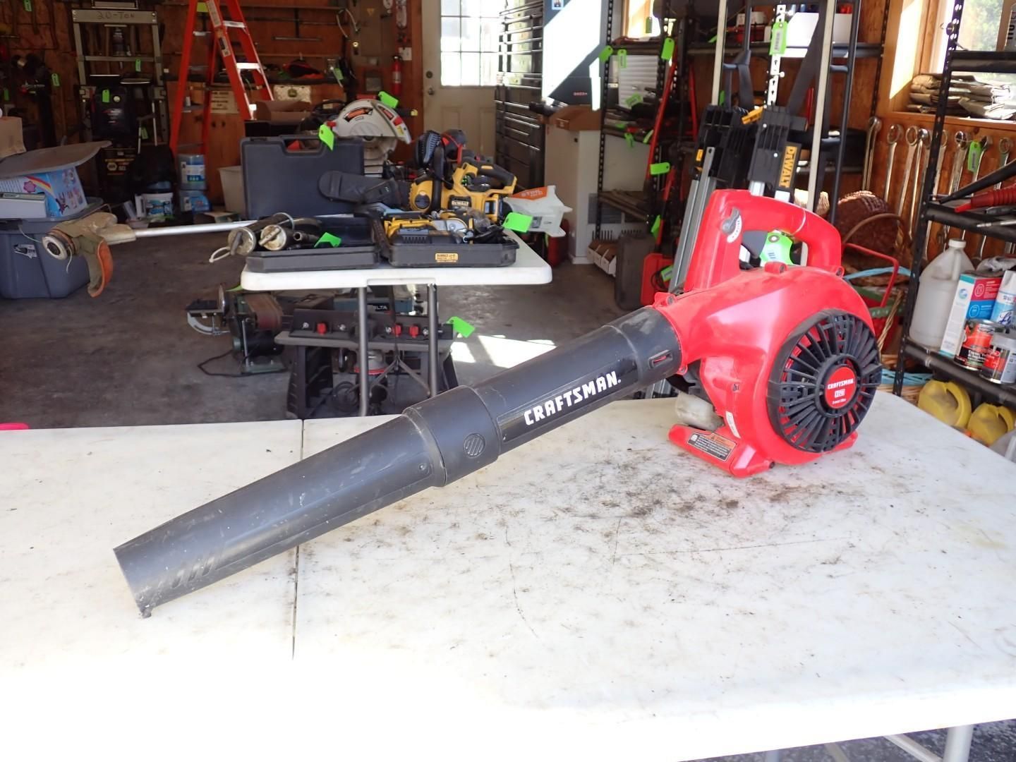 Red leaf blower on a workbench in a garage, with a black nozzle and red motor housing.