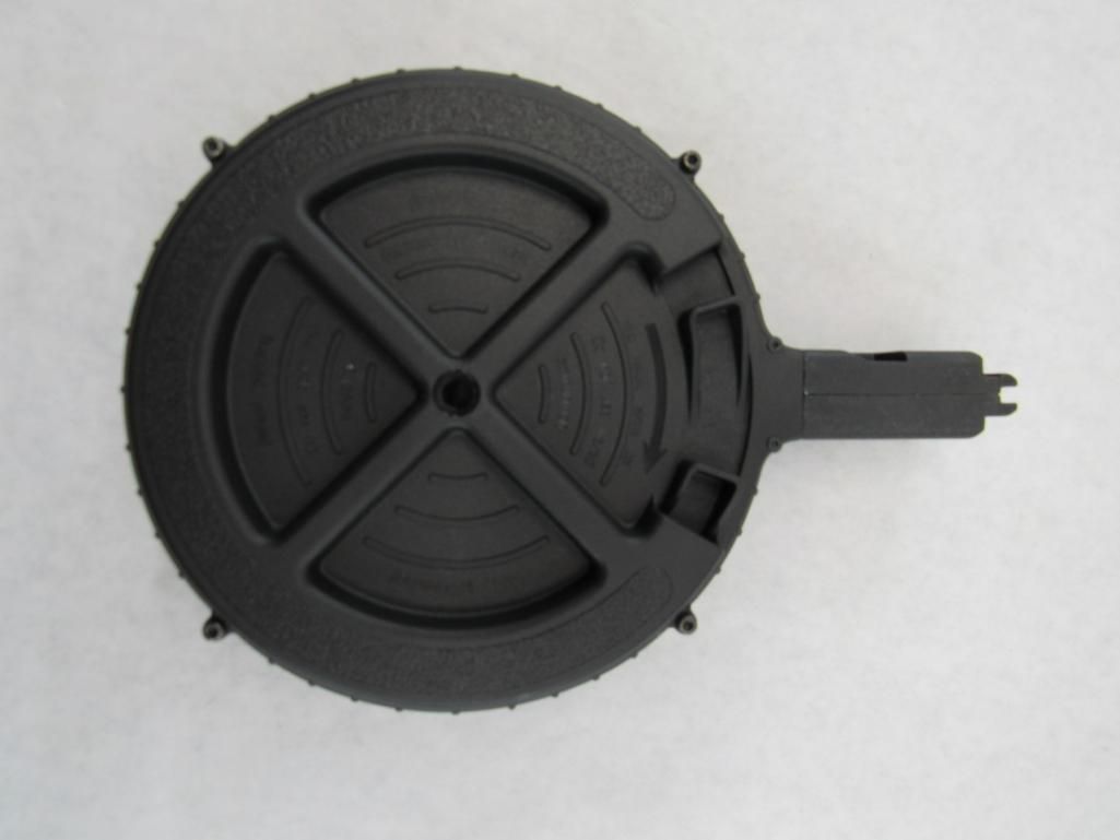 Black, circular drum magazine for a firearm, with central cross pattern and handle.