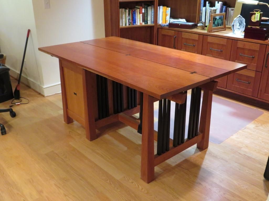 Wooden desk with a honey-colored top, dark support slats, and a cabinet, in a room with hardwood flooring.