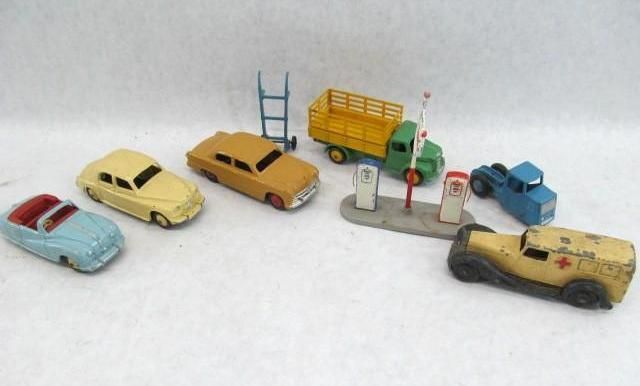 A collection of vintage toy cars: convertible, sedan, truck, ambulance, and a blue pickup, with a gas station.