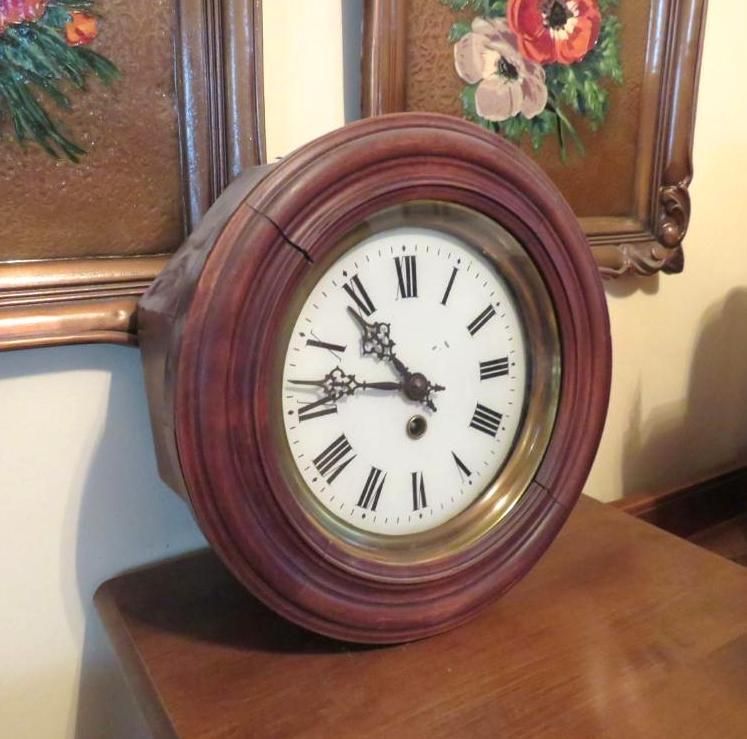 Round wooden clock with white face and Roman numerals on a wooden table.
