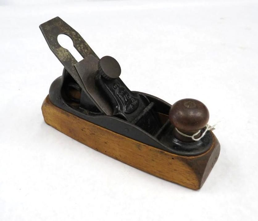 Small, black and wood hand plane tool, with a metal blade and wooden knob, on a white surface.