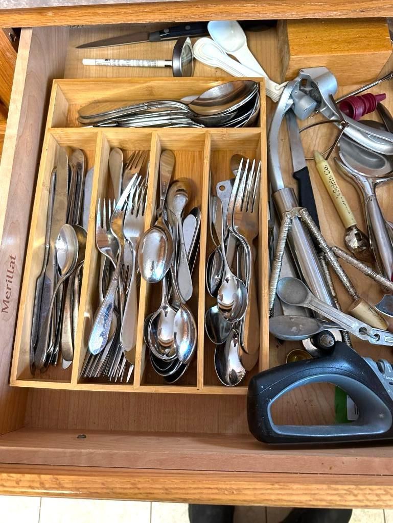 A drawer filled with silverware: forks, spoons, and knives. A wooden organizer separates the utensils.