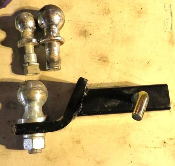 Three trailer hitch balls, one mounted on a black bracket, all on a light brown surface.
