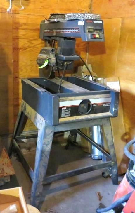 Black and gray radial arm saw on a stand, indoors.