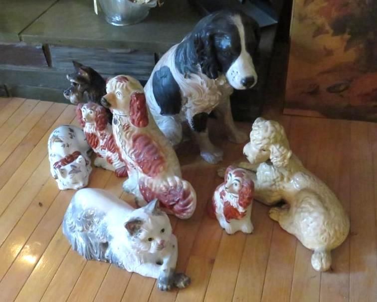 Collection of painted dog and cat figurines on wooden floor. A black and white dog is largest.