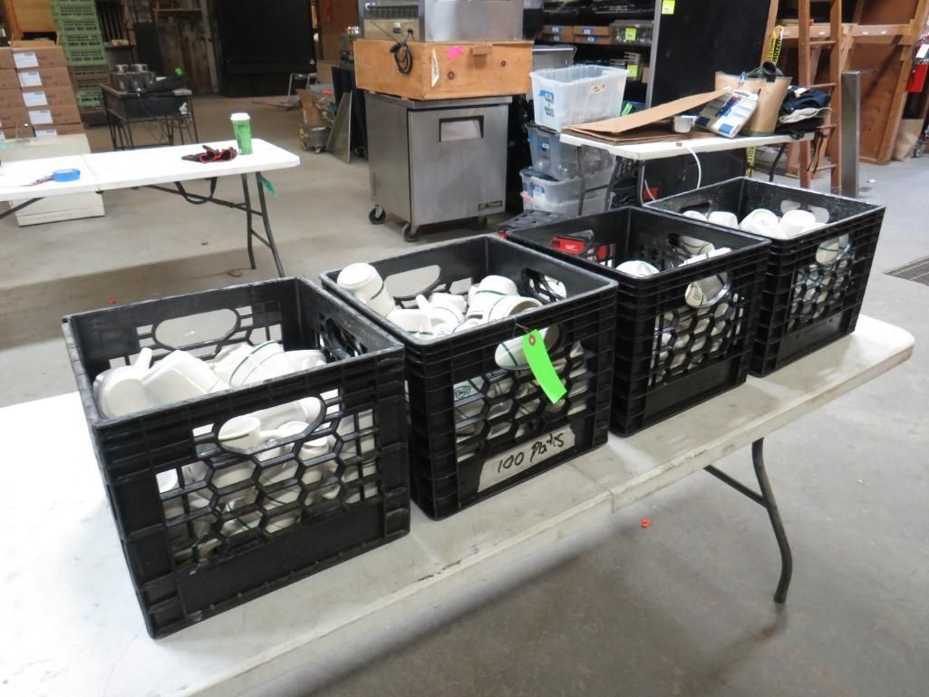 Four black crates filled with white objects sit on a white table in a warehouse.