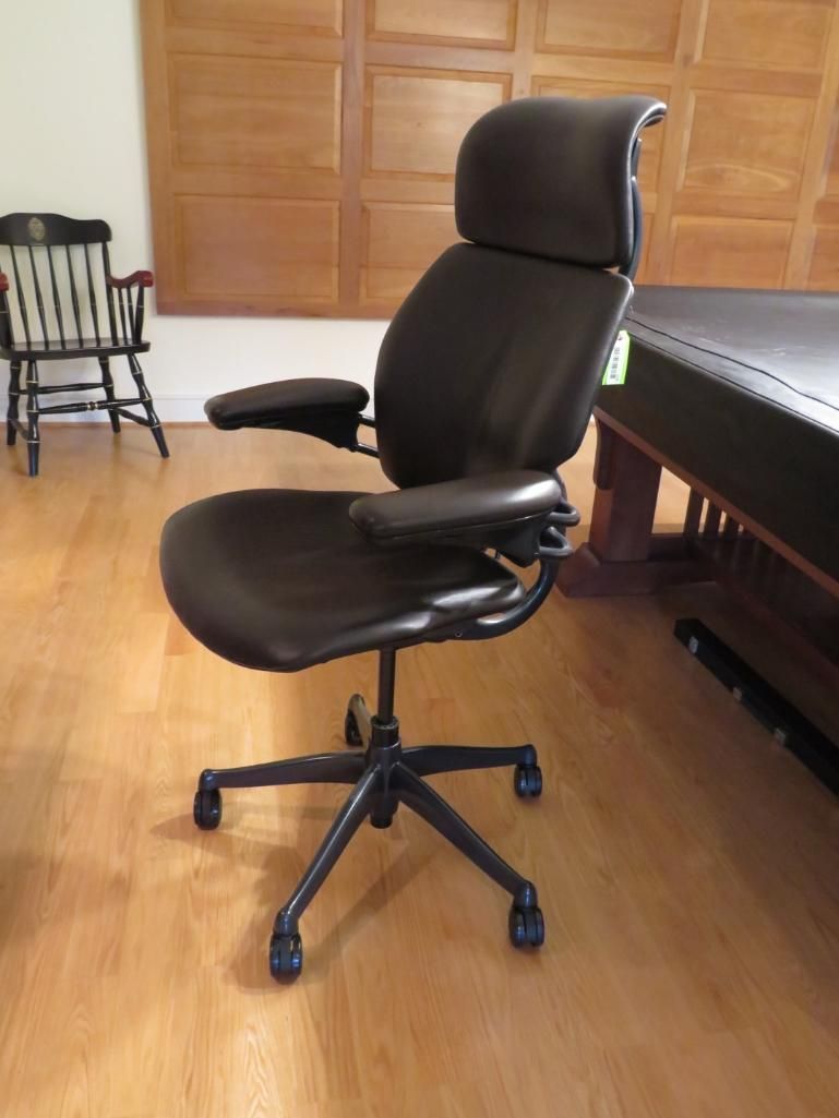 Black ergonomic office chair with headrest, on a wood floor.
