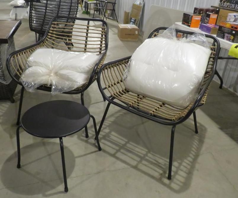 Two rattan chairs with cushions, next to a small black side table, indoors.