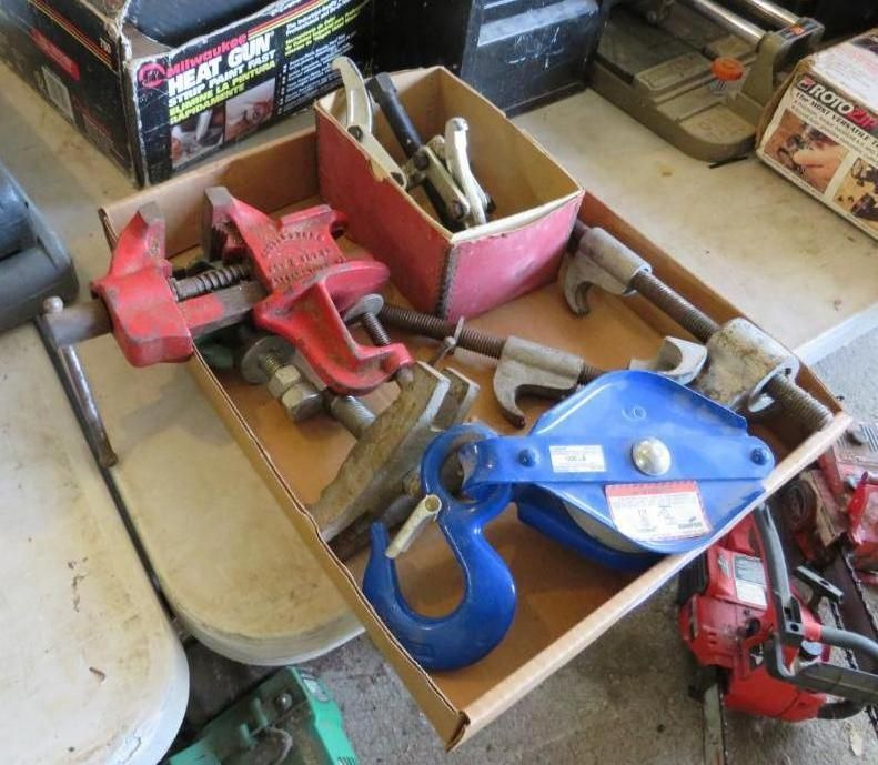 Tools in cardboard box: red vise, blue pulley, and other metal tools.