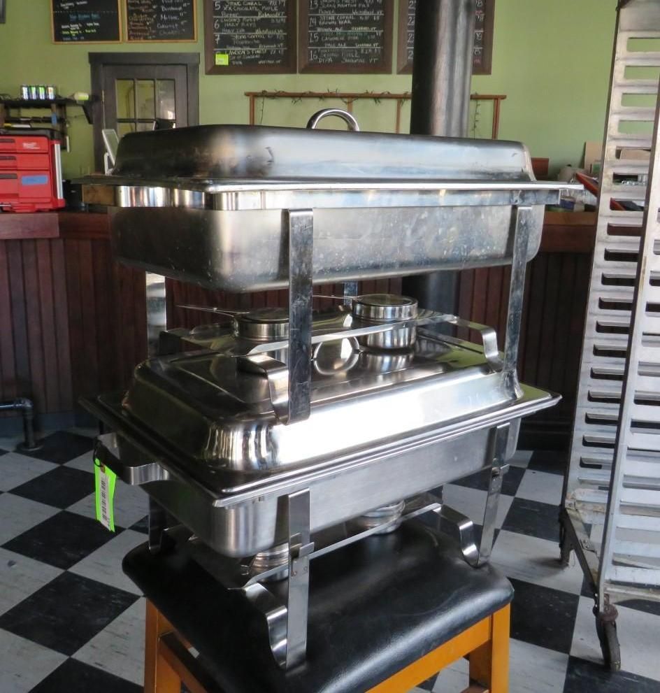 Two-tiered stainless steel chafing dishes on a wooden stool in a restaurant or store.
