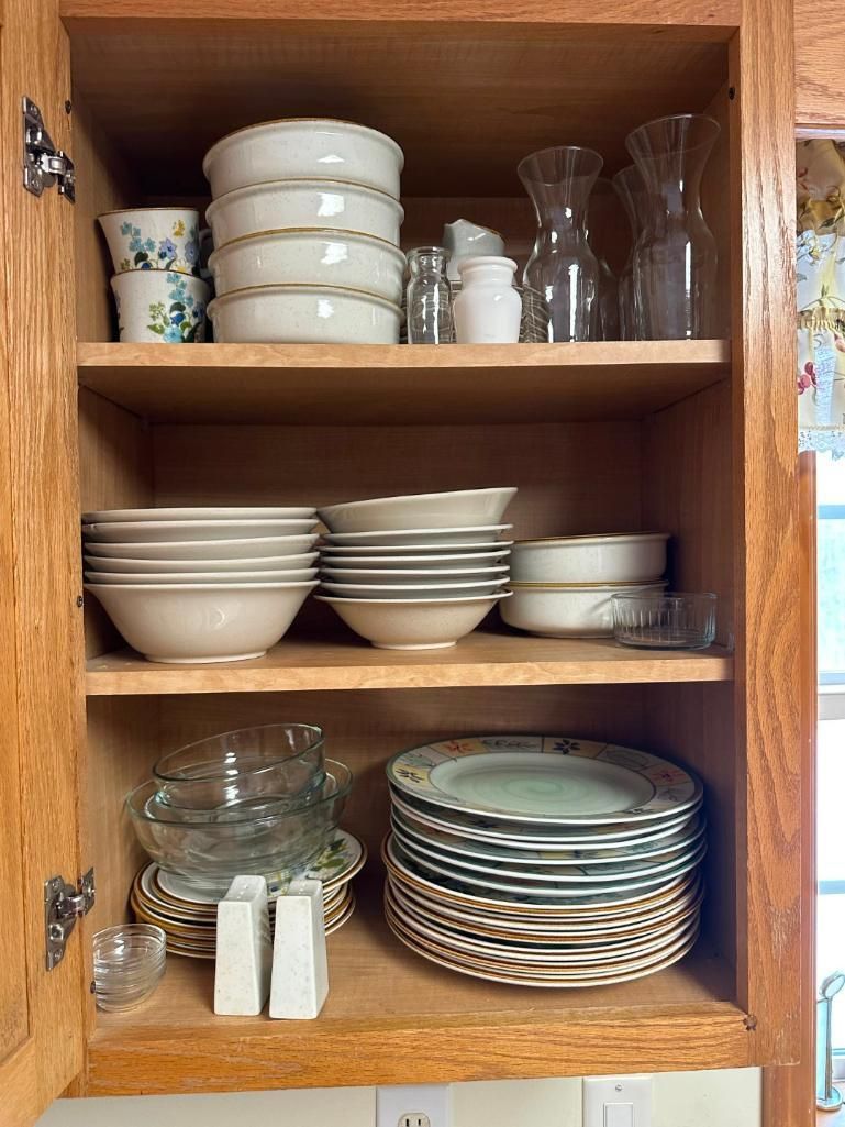 Wooden cabinet filled with stacked dishes, bowls, glasses, and pitchers.