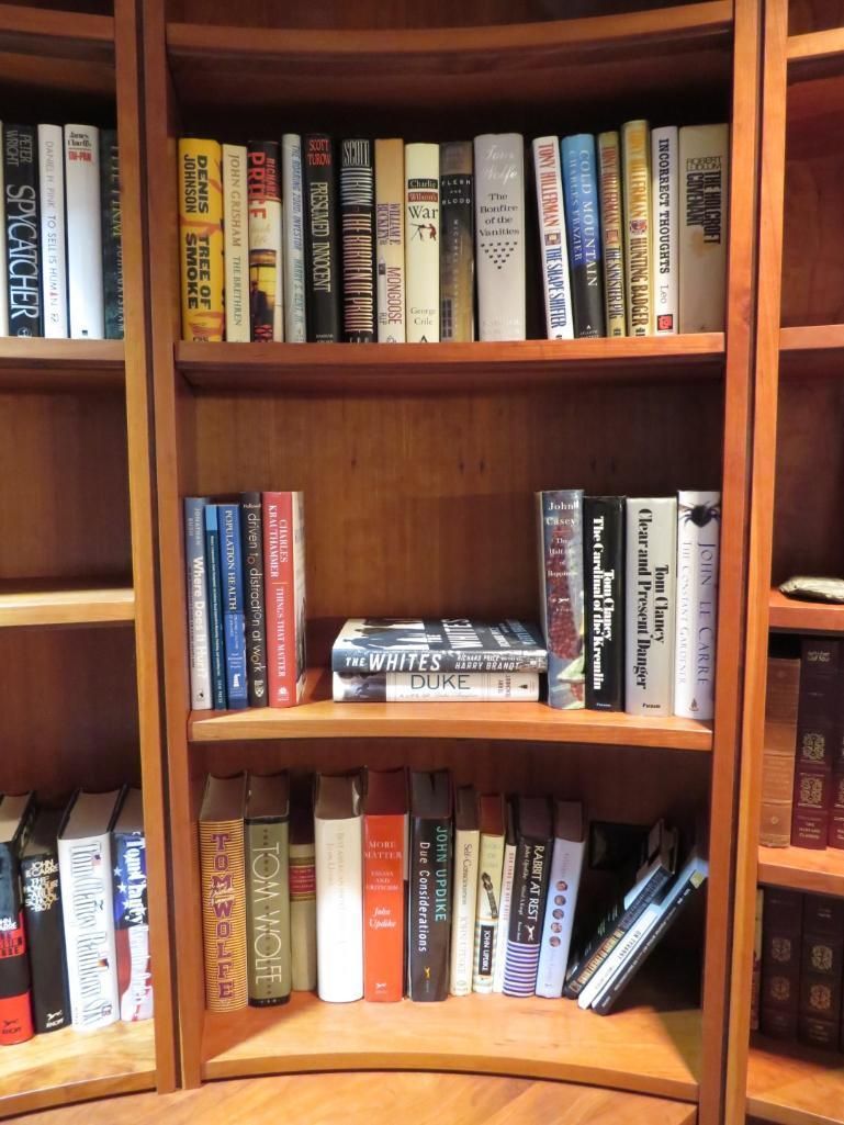 Wooden bookshelf filled with various books, DVDs, and some leaning items.