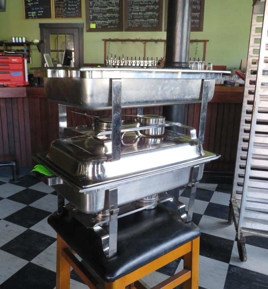 Stacked stainless steel chafing dishes on a stool in a restaurant.