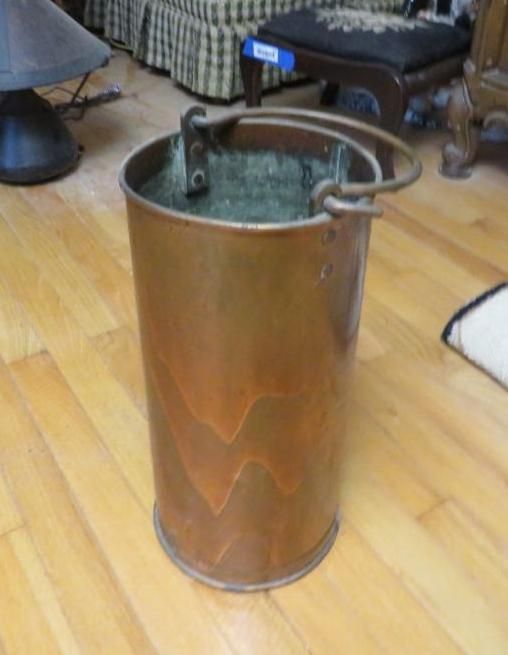 Copper bucket with handle, standing on a hardwood floor.