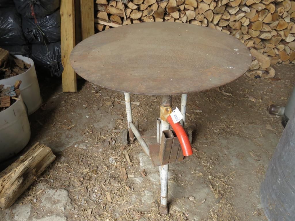 Round metal table with a white, metal frame, set in a wood shed.