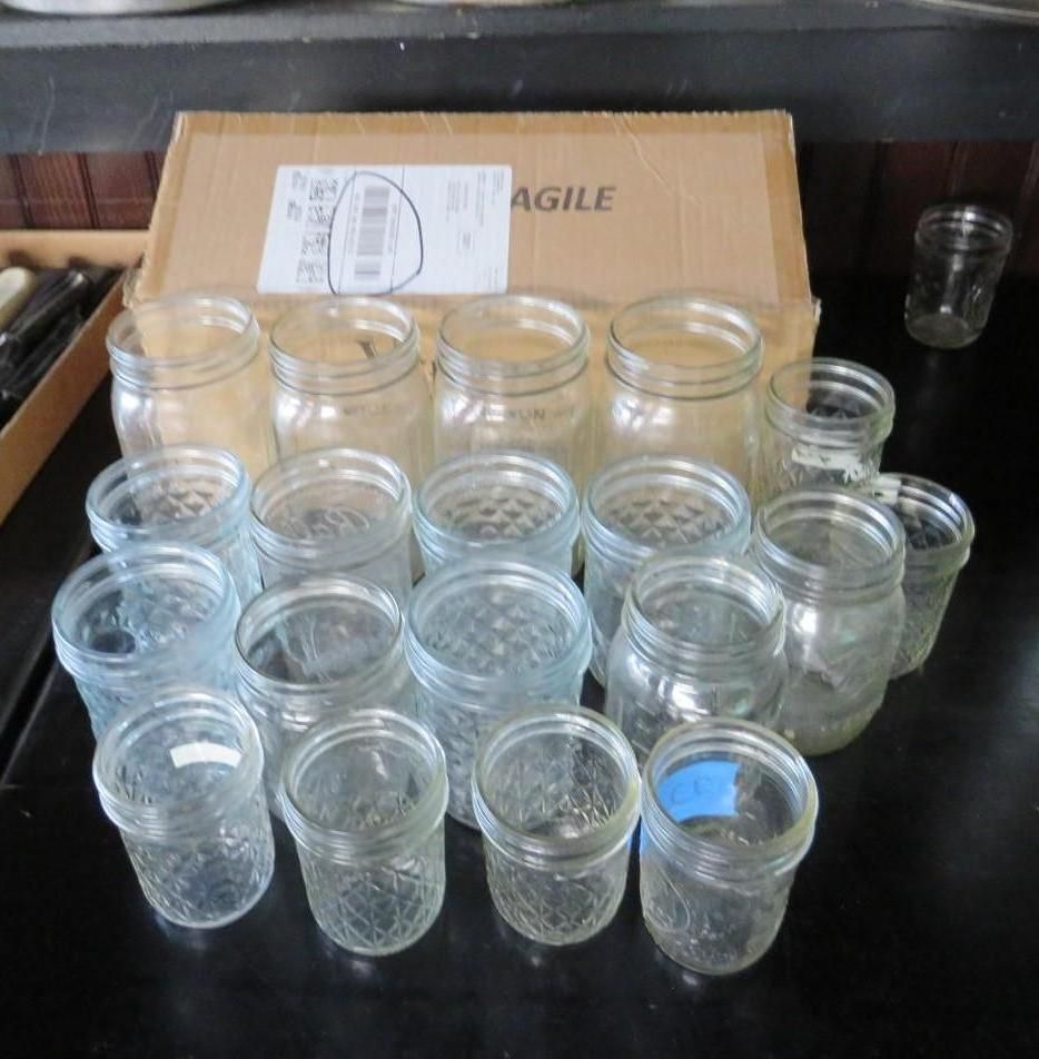 A group of glass mason jars, some with lids, are arranged in front of a cardboard box on a dark surface.