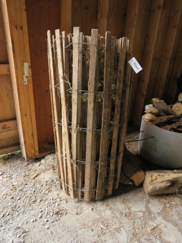 Cylindrical wooden fence section, tied together with wire, standing indoors.
