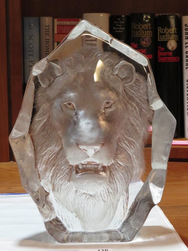 Clear crystal lion head sculpture in a bookshelf setting.