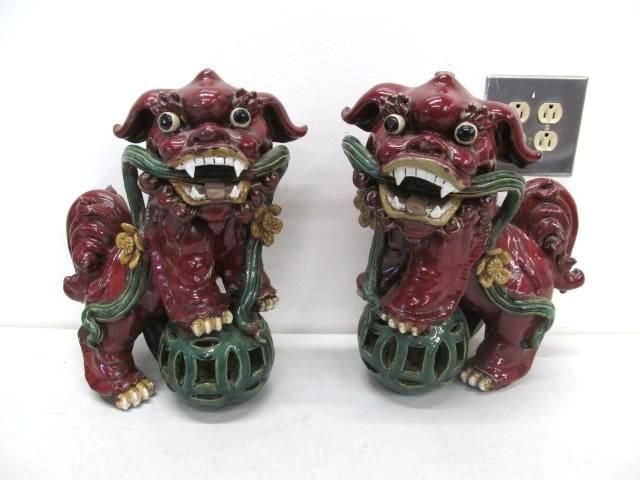 Two red ceramic guardian lion statues, holding orbs, with green and gold accents.